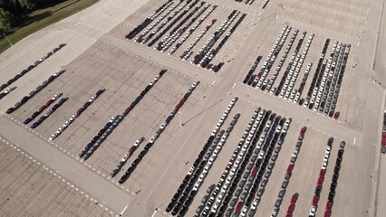 Parked new cars at the car automotive plant manufacturer lot. Electric hybrid cars vehicle factory. Aerial. Almost empty stock. Broken supply chain and chip shortage lead to car shortage availability