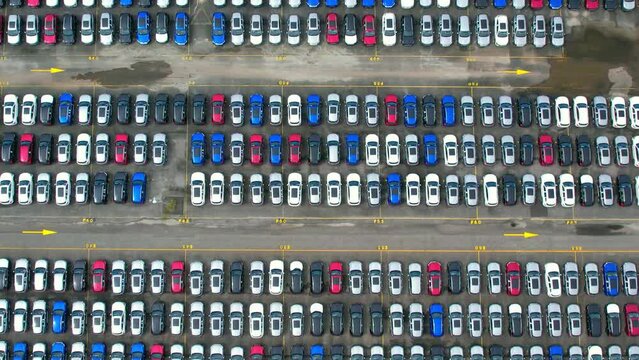 Drones flying above factory parking lot, new cars unsold. import and export industry. automotive industry. 4K
