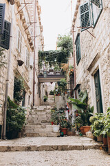 Fototapeta na wymiar Dubrovnik, Croatia - September 21, 2021: Narrow dark street with greenery in old medieval town, listed UNESCO World Heritage Sites. King's Landing, capital of Seven Kingdoms in show Game of Thrones