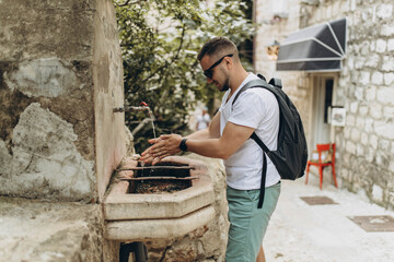 Man tourist, traveler wash his hands outside the street in old medieval tap and sink. Old town was...