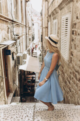 Beautiful blonde lady tourist, traveller in blue dress and straw hat walks along narrow streets in Dubrovnik, Dalmatia, Croatia. Old town was listed as UNESCO World Heritage Sites in 1979 in Europe