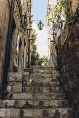 Naklejka premium Dubrovnik, Croatia - September 21, 2021: Narrow dark street with greenery in old medieval town, listed UNESCO World Heritage Sites. King's Landing, capital of Seven Kingdoms in show Game of Thrones