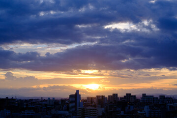 Fototapeta na wymiar 厚い雲に覆われた東の空から太陽が姿を表し。高層ビルがシルエットで浮かび上がる。早朝神戸市内より芦屋大阪方面を臨む。