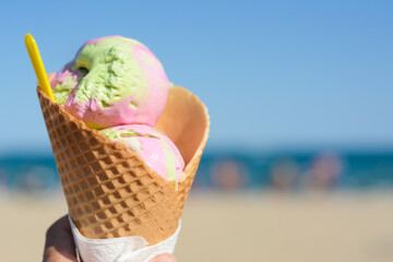 Little girl holding waffle cone with scoops of delicious colorful ice cream at beach on sunny...