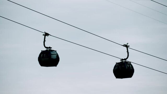Ropeway, cable car cabins silhouettes are moving against gray sky in Batumi, Georgia - aerial rope transit, gondola lift - overcast. Tourism, cableway, sightseeing and public transportation concept