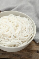 Bowl with cooked rice noodles on wooden table, closeup