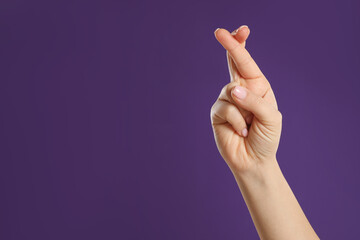 Woman holding fingers crossed on purple background, closeup with space for text. Good luck...