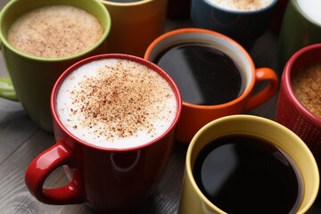 Many different cups with aromatic hot coffee on wooden table, closeup