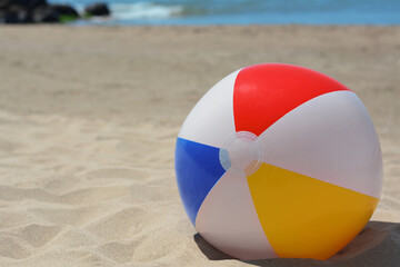 Colorful beach ball on sand near sea, space for text
