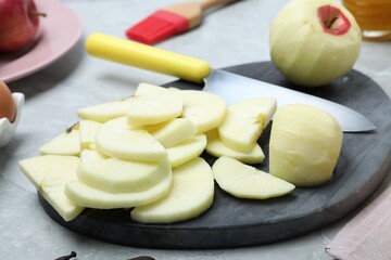 Cut fresh apple with knife and board on grey table, closeup. Baking pie