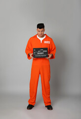 Fototapeta na wymiar Prisoner in orange jumpsuit with mugshot letter board on grey background