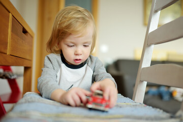 Cute toddler boy playing with red toy car. Small child having fun with toys. Kid spending time in a cozy living room at home.