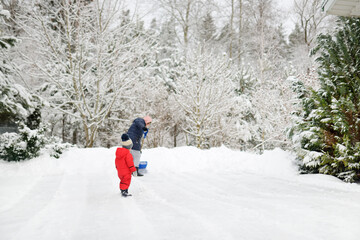 Senior woman and her little grandson shoveling snow off a walkway after massive snowfall. Small...