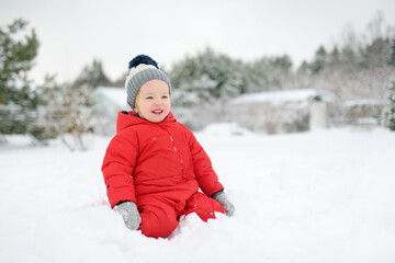 Fototapeta na wymiar Adorable toddler boy having fun in snow covered park on chilly winter day. Child exploring nature.