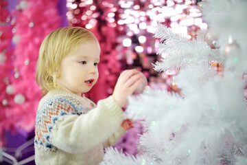 Fototapeta premium Happy little toddler boy playing with Chistmas lights in a cozy living room on Christmas eve. Celebrating Xmas at home.