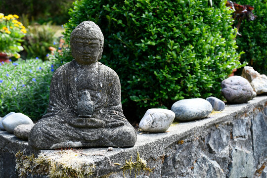 An image of a small stone Buddha statue in a tranquil flower garden. 