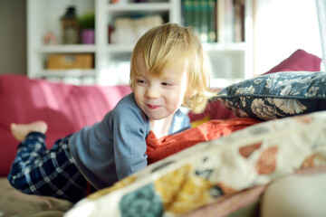 Cute toddler boy sitting on a couch. Small child spending time in a cozy living room at home.