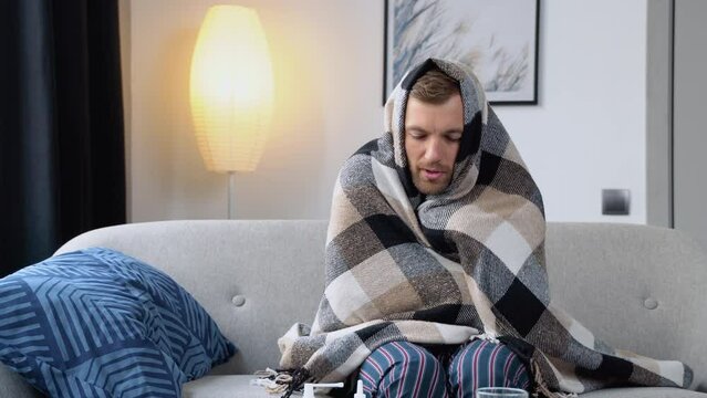 Young man suffering from a common cold and flu or allergy sit at home wrapped in blanket while he have a strong headache pain. Healthcare concept