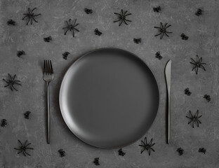 Halloween black table setting. Empty black plate, decorative spiders on a gray background. Mockup or template. Copy space, top view, flat lay.