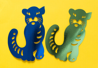two metallic foil paper silhouettes of big cats (tiger or jaguar) isolated on yellow paper