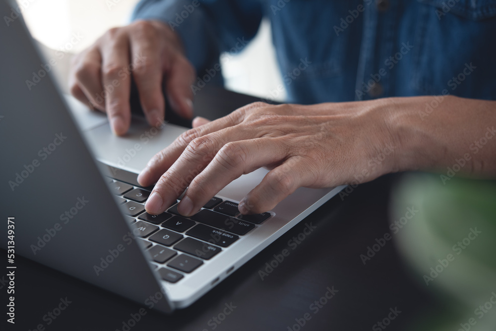 Wall mural Closeup of a business man's hands working and typing on laptop computer keyboard on wooden table