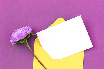 White blank card, yellow envelope and flower on purple background. Minimal style. Top view Flat lay Mockup