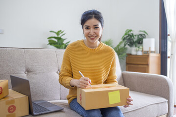 Business Asian women sit on sofa use laptop computer checking customer order online shipping box at home. Starting Small business entrepreneur SME freelance. Online business, Work at home SME concept.