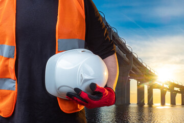 Builders helmet in hand. Builders helmet in front of bridge. White helmet for working builders....