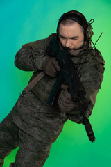 soldier in the studio on a green background with colored light. a man in military uniform with a gun, rifle or machine gun. military. airball player