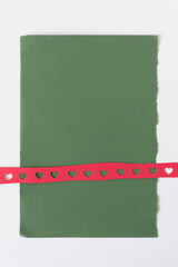 red paper ribbon with heart shapes on green paper with torn edge