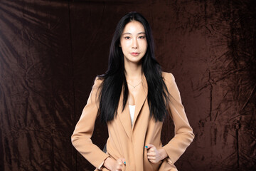Haft body portrait of beautiful transgender 20s asian woman express feeling smiling confidently on brown background. Business Female smart look blazer has wind blow throw her hair in air, copy space - obrazy, fototapety, plakaty