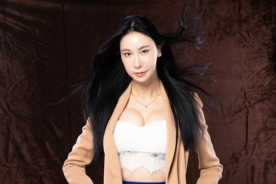 Haft body portrait of beautiful transgender 20s asian woman express feeling smiling confidently on brown background. Business Female smart look blazer has wind blow throw her hair in air, copy space