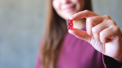 Closeup image of a young woman holding and showing at a red jelly gummy bear