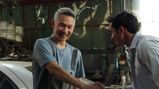 Handshake good deal and greeting. Asian young man customer talking with owner and mechanic worker at car repair service and auto store shop.