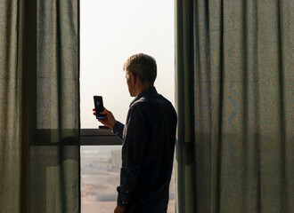 Silhouette of a man with mobile phone at the window. Concept
