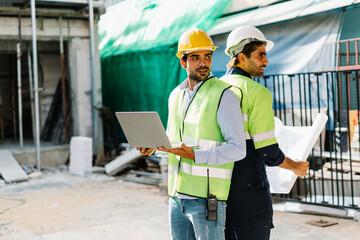 Working Safety at Workplace Concept, construction worker and contractor wearing protective gear holds a laptop and a blueprint on a building site