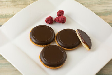 Obraz na płótnie Canvas Cookies with dark chocolate and raspberry filling on white snack plate