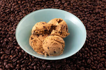 Coffee ice cream with espresso chocolate chips in blue dessert bowl on background of roasted coffee beans