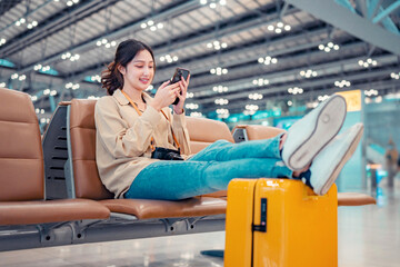 Happy asian tourist woman using mobile phone and put leg on suitcase traveling between waits for...