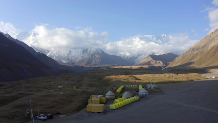 Base Camp under Lenin Peak at dawn. View of yellow tents, containers and national yurts. The amazing nature of Kyrgyzstan.