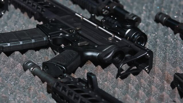 Firearm in specialistic case filled with grey foam. Black guns and rifles lying down. Beige collimator at the end. Shooting range concept. High quality 4k footage