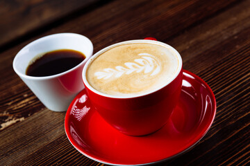 Coffee in a red cup with milk and latte art and coffee in a white cup on a table