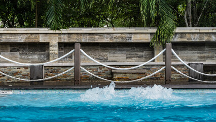The swimming pool is fenced with a rope railings. The clear blue water is bubbling. The green...