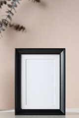 blank black photo frame mockup with eucalyptus brancch at peach wall