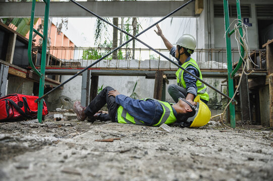 First aid support accident at work of builder worker in construction site. Accident falls from the scaffolding on floor, Foreman help employee accident with first aid bag and wave hand to team help.