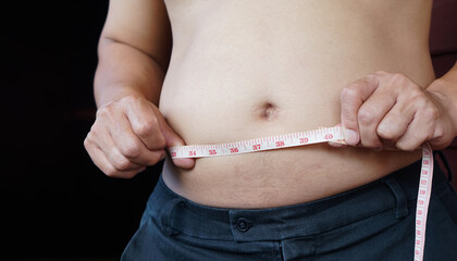 Closeup man is  measuring his fat belly with measurement tape for 40 inches. Concept : overweight....