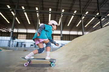 asian child skater or kid girl playing skateboard or ride surf skate up to wave ramp or wave bank to fun bottom turn in skate park by extreme sports surfing to wear helmet knee support for body safety