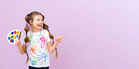 A little artist points to your advertisement on a pink isolated background. The child holds a palette of colorful paints and brushes for drawing. Art courses for schoolchildren.