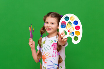 A little artist with a multi-colored palette of paints and brushes for drawing on a green isolated...