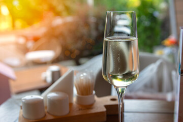 a glass of champagne is on the table of an outdoor cafe in the background is a park street, the greenery of trees and the setting sun. A relaxed and comfortable pastime